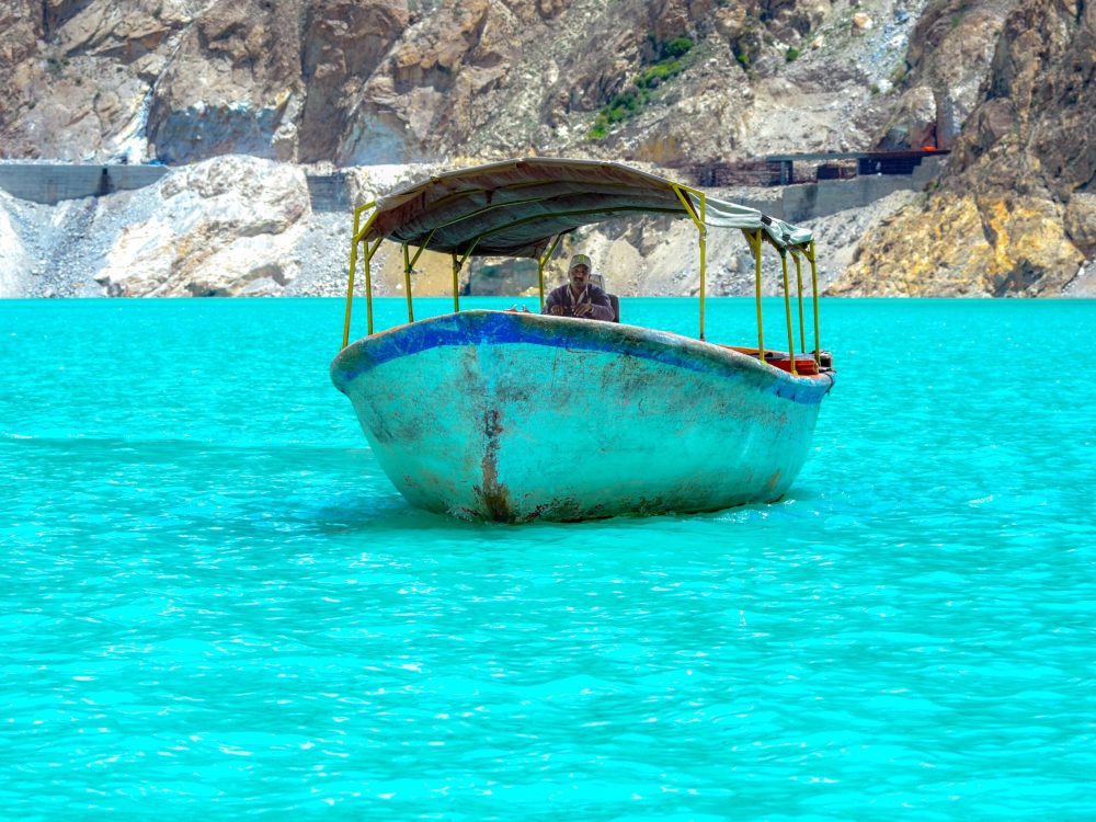 A rustic motorboat cruising through vibrant turquoise water against a scenic mountainous backdrop.