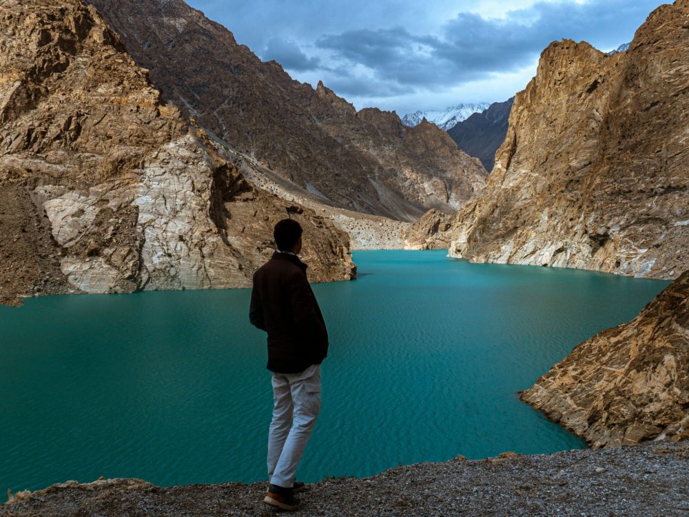 A man gazes at the stunning turquoise waters of Attabad Lake surrounded by majestic mountains in Hunza, Pakistan.