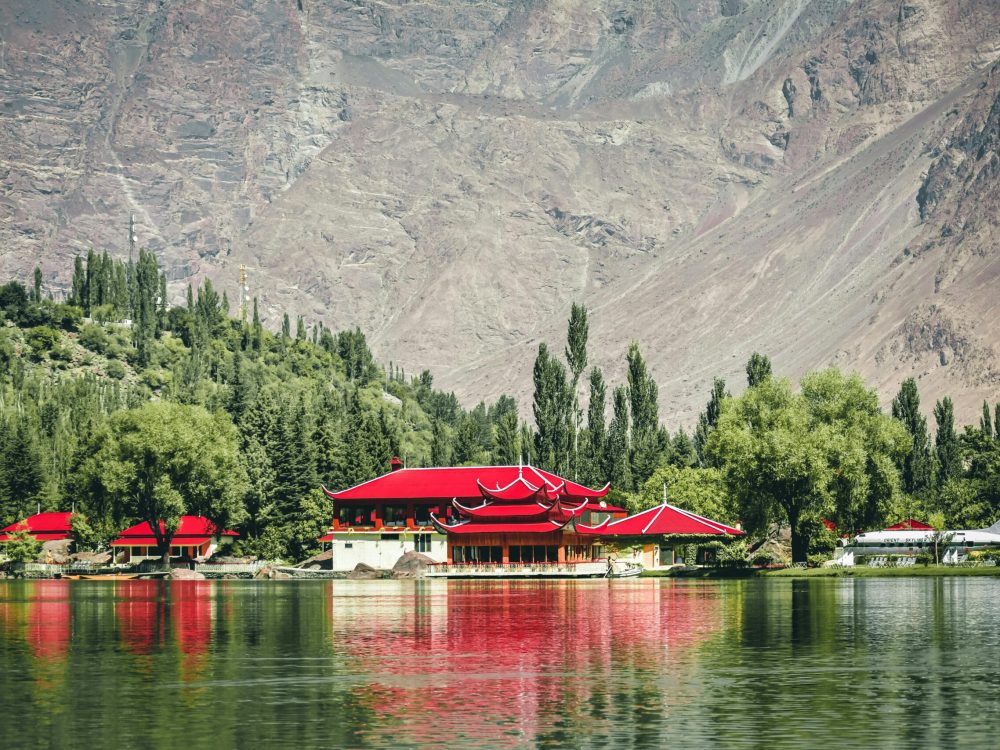 Stunning lake view with traditional architecture and vibrant red roofs framed by mountains and trees.